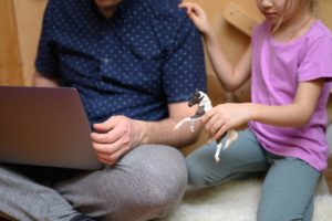 a man working from home using a laptop and his little daughter playing with childrens toys concept of t20 4exjAA scaled 1