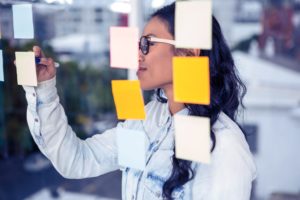 asian woman writing on sticky notes on glass wall P2JJKQJ scaled 1